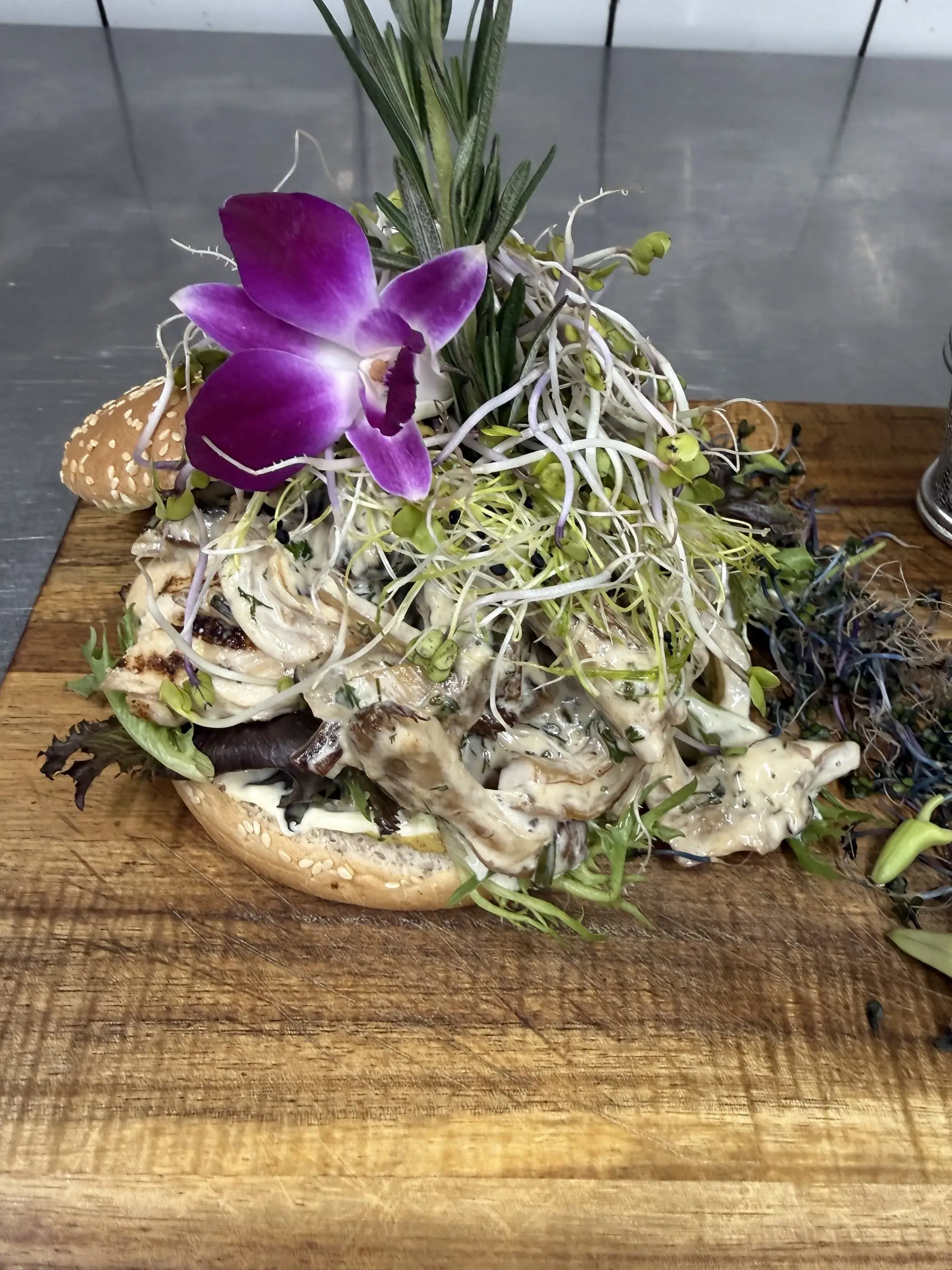 Nærbillede af en gourmetburger med svampe, spirer og en orkidé
