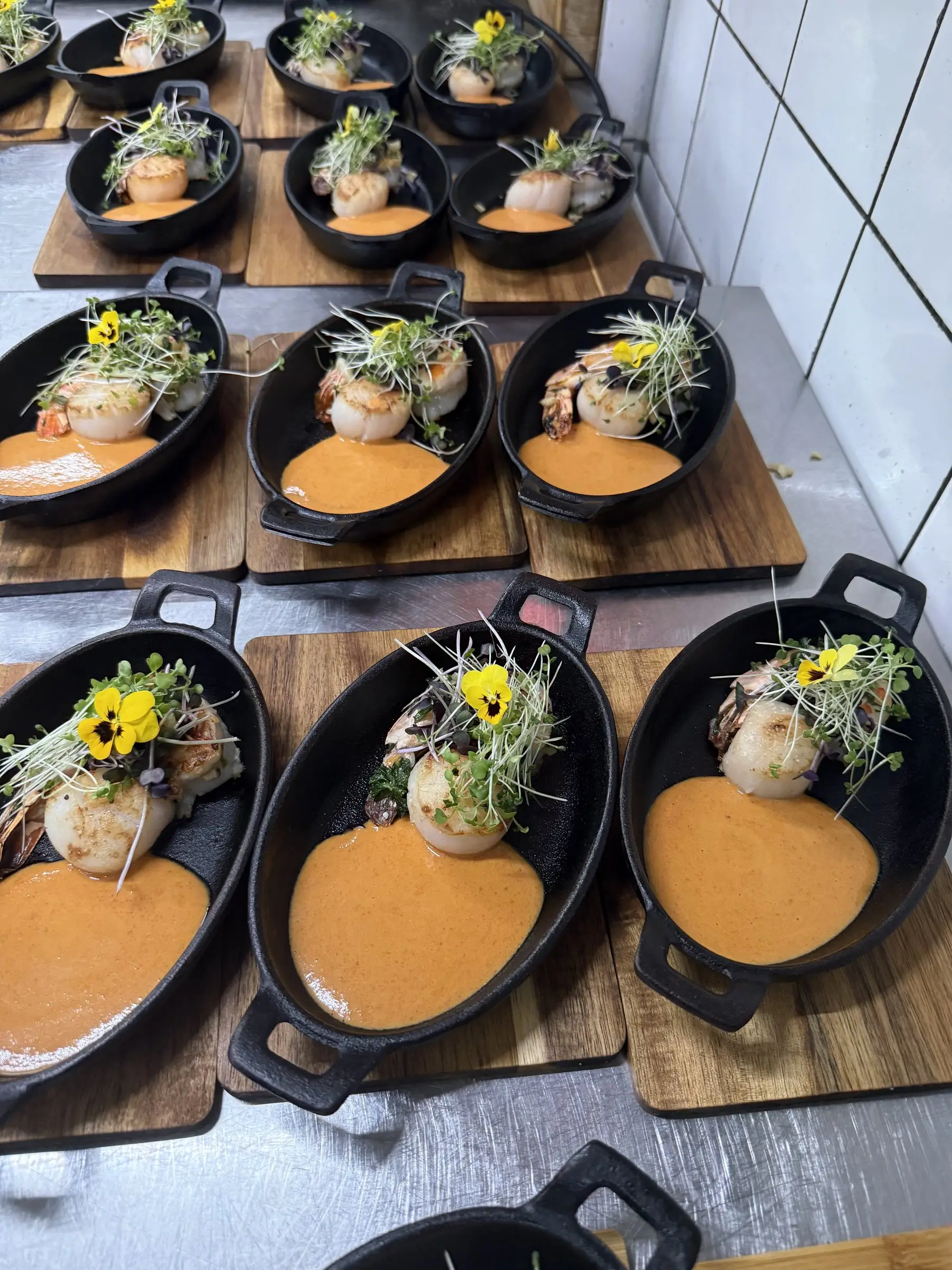 Kammuslinger i små jerngryder med hummersauce og spiselige blomster