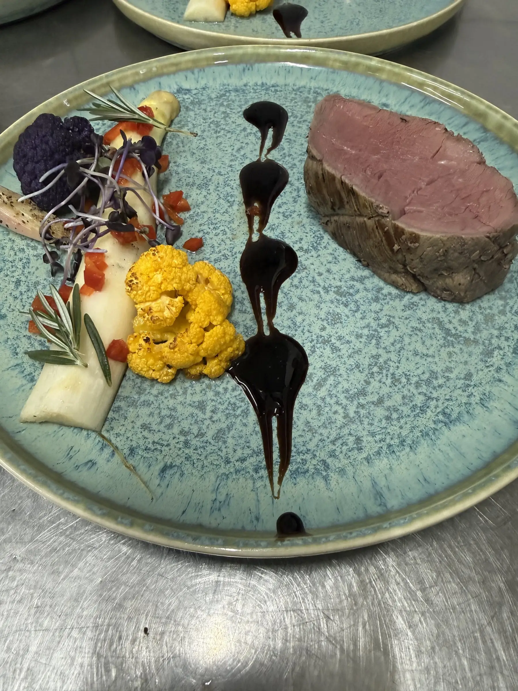 Oksemørbrad med blomkål, rødbede og sauce på en blå tallerken