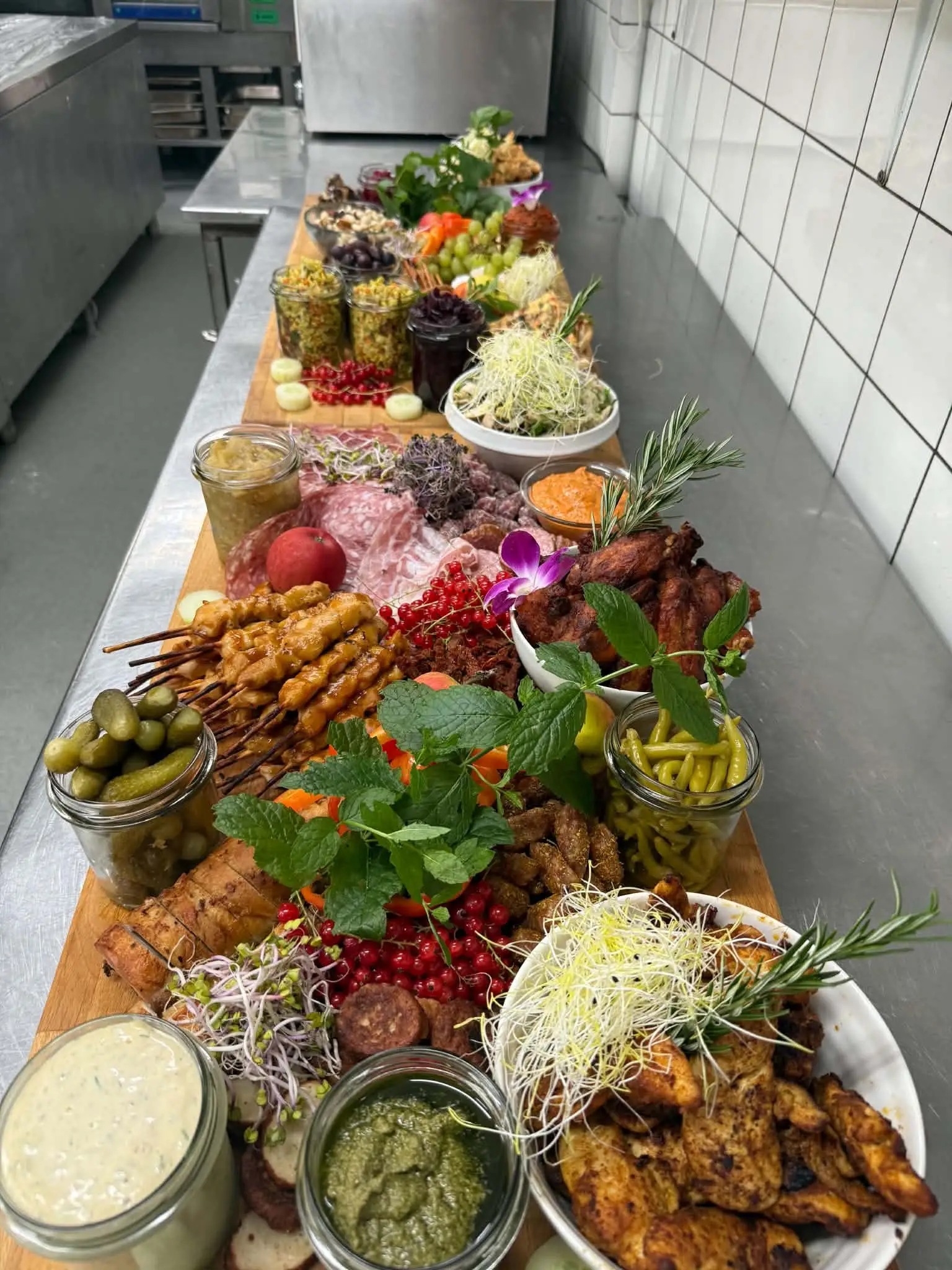 Langt tapasbord i køkkenet med spyd, dip, pickles og salater